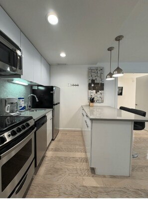 A modern kitchen with stainless steel appliances, a central island, pendant lighting, and a tiled backsplash.