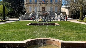 A historic building with a central fountain, surrounded by a well-maintained lawn and a formal garden.
