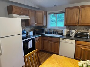 A kitchen with wooden cabinets, a microwave, a toaster, a sink, and a window with a view of greenery.