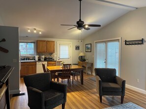 A kitchen with wooden cabinets, a dining table with chairs, a ceiling fan, and a window with blinds.