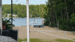 Una spiaggia sabbiosa con un'area giochi, una barriera di corde e un lago sullo sfondo con delle case.