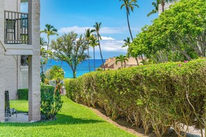 A coastal building with a balcony, lush greenery, and a view of the ocean. - New Listing Discount! Beautiful Ground Floor Tropical Oasis with Ocean View! (Kihei)