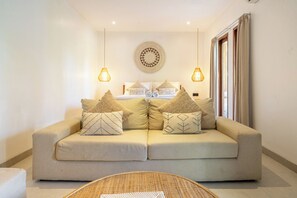 A neutral-toned living room with a sofa, two hanging lamps, a round wall decoration, and a window with curtains.