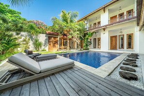 A poolside area with lounge chairs, a wooden deck, and a building with balconies.