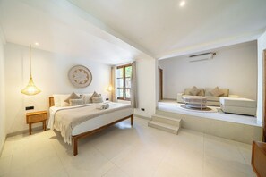 A spacious bedroom with a large bed, bedside lamps, a wall-mounted air conditioner, and a view of the outdoors.