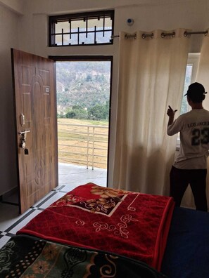 Une chambre avec une grande fenêtre, une porte en bois et une personne debout près de la fenêtre.