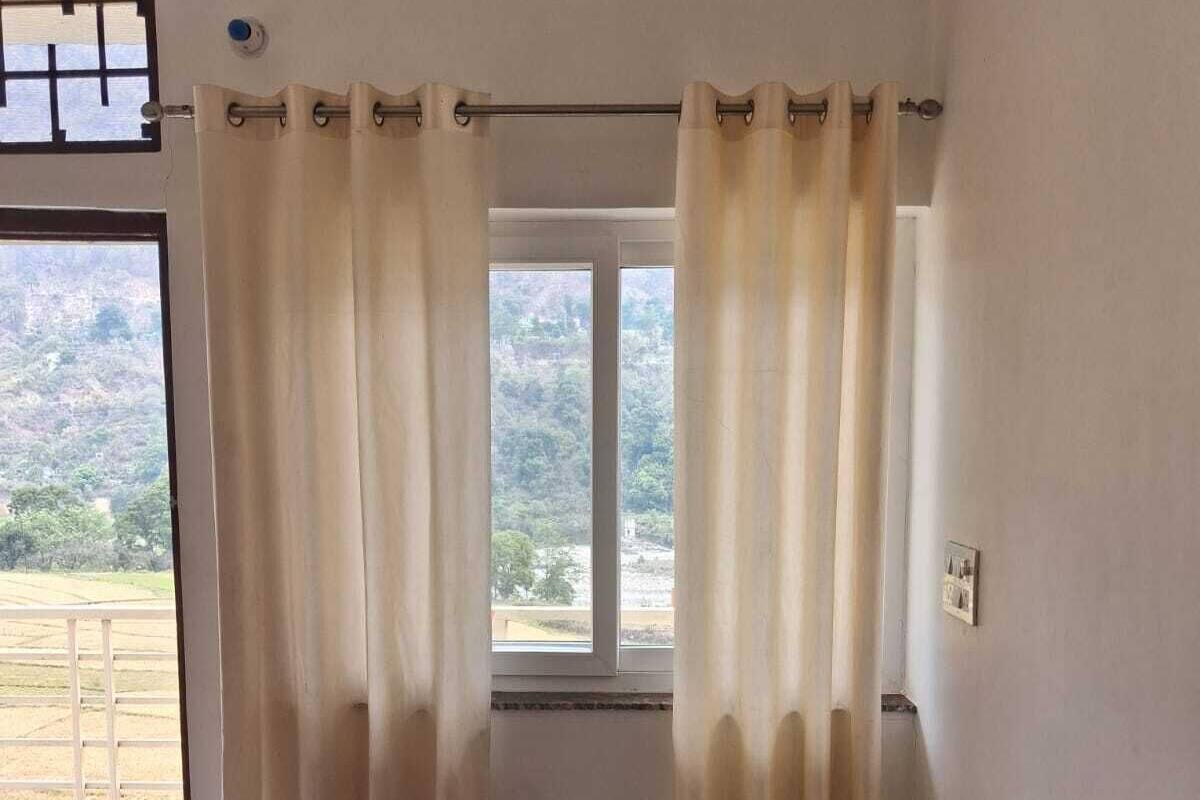 Quarto com cama, cortinas, janela e vista para uma paisagem.