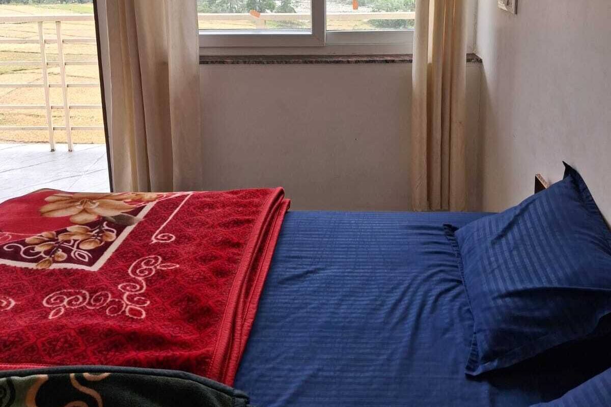 Um quarto com cama, cortinas, janela e vista para uma paisagem montanhosa.
