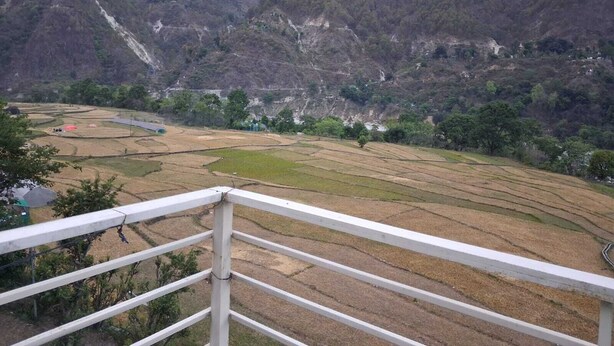 A mountainous landscape with terraced fields and a white railing in the foreground.