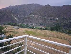 A mountainous landscape with terraced fields and a white railing in the foreground. - Hotel CSR Palace (Karnaprayag)