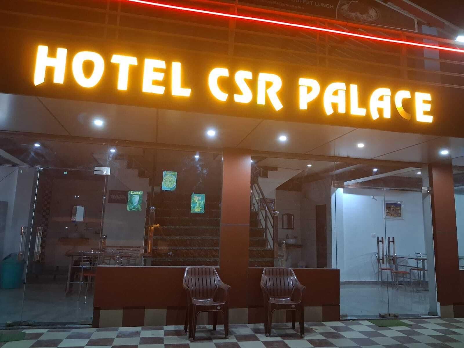 Entrada de un hotel con un letrero de neón que dice 'HOTEL CSR PALACE', fachada de vidrio y un piso con diseño de cuadros.