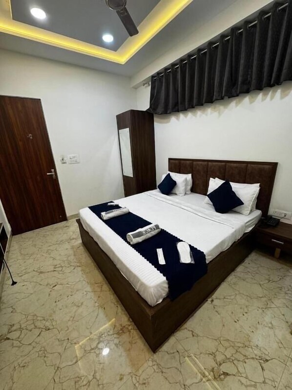 Una cama bien hecha con almohadas y una manta, una mesita de noche con un teléfono, un armario de madera y un ventilador de techo.