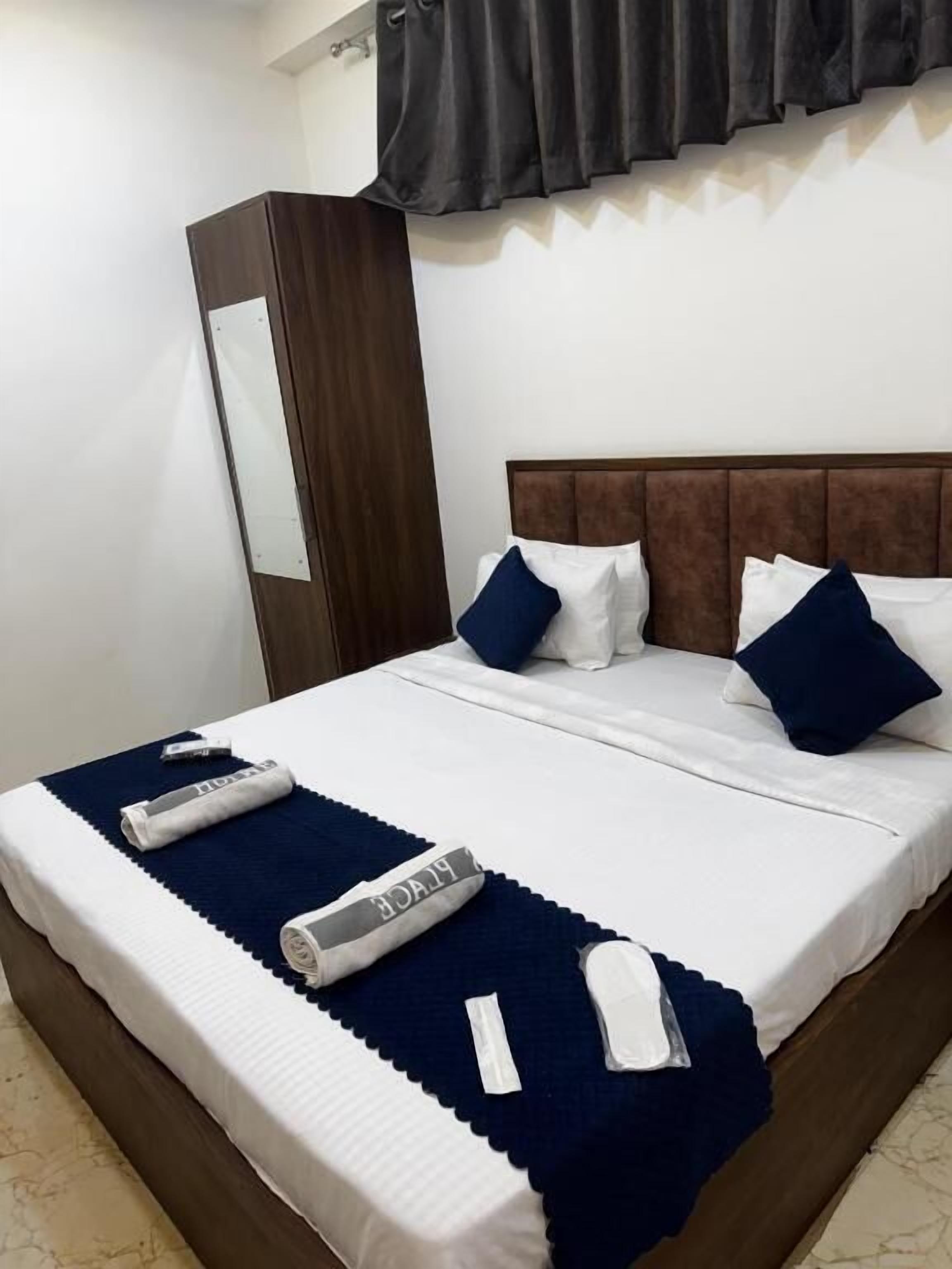 Una cama bien hecha con ropa de cama blanca y azul, un cabecero marrón oscuro y un armario de madera.