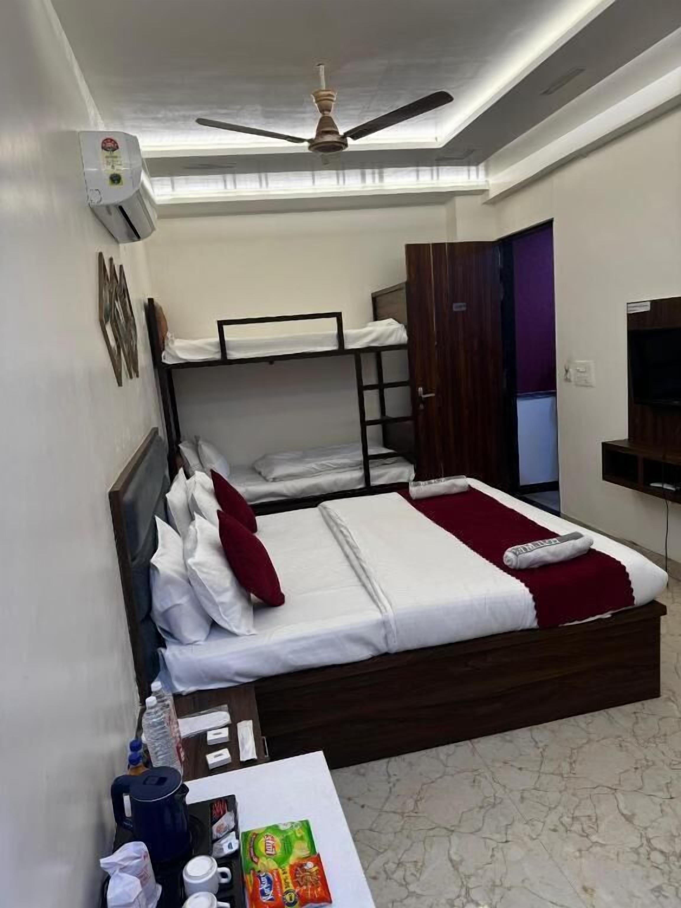 Ein Hotelzimmer mit Etagenbetten, einem Schreibtisch mit Toilettenartikeln, einem Deckenventilator und einem Fernseher.