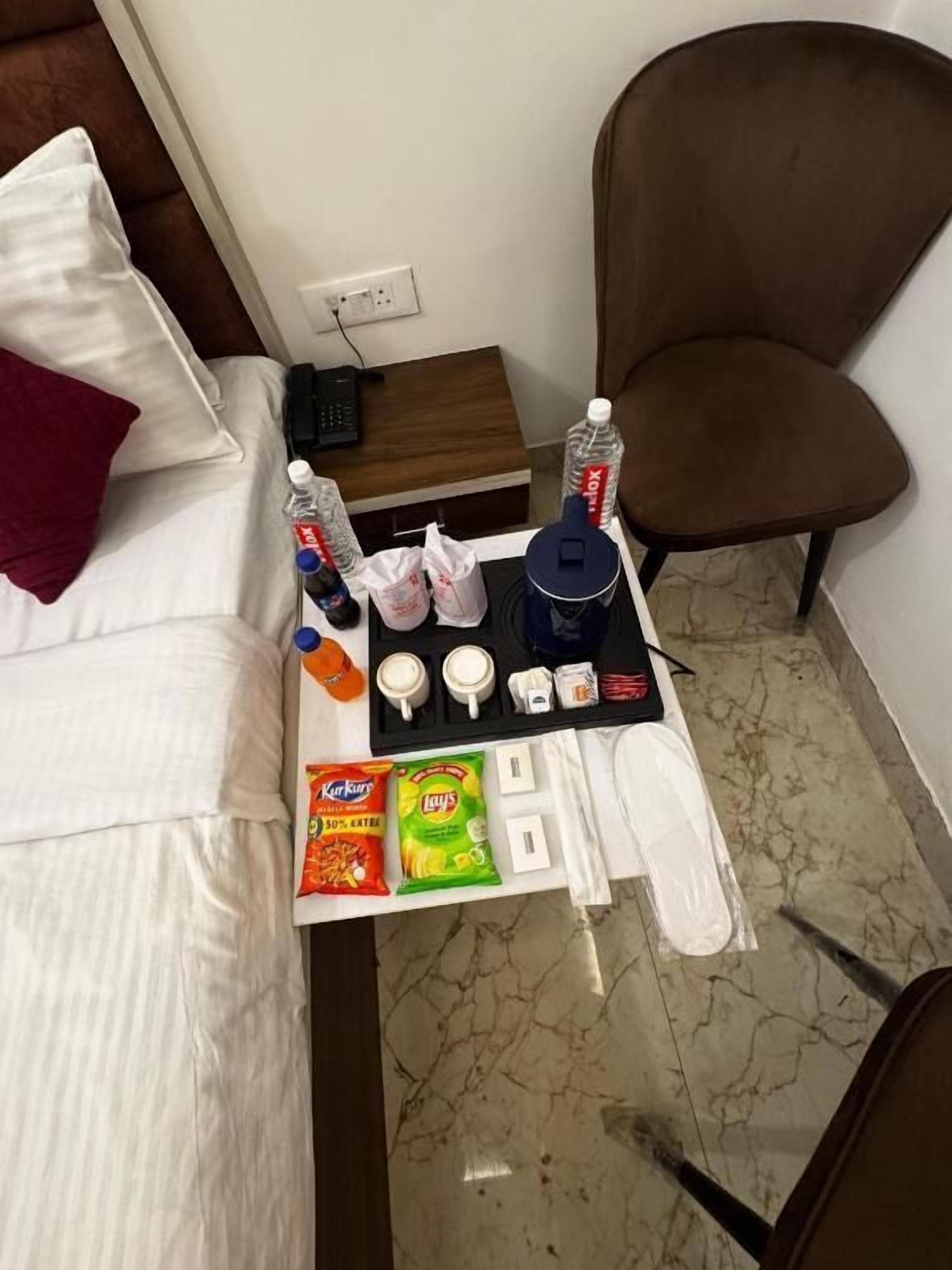 Una habitación de hotel con una cama, una mesita con aperitivos, una silla y una cafetera.