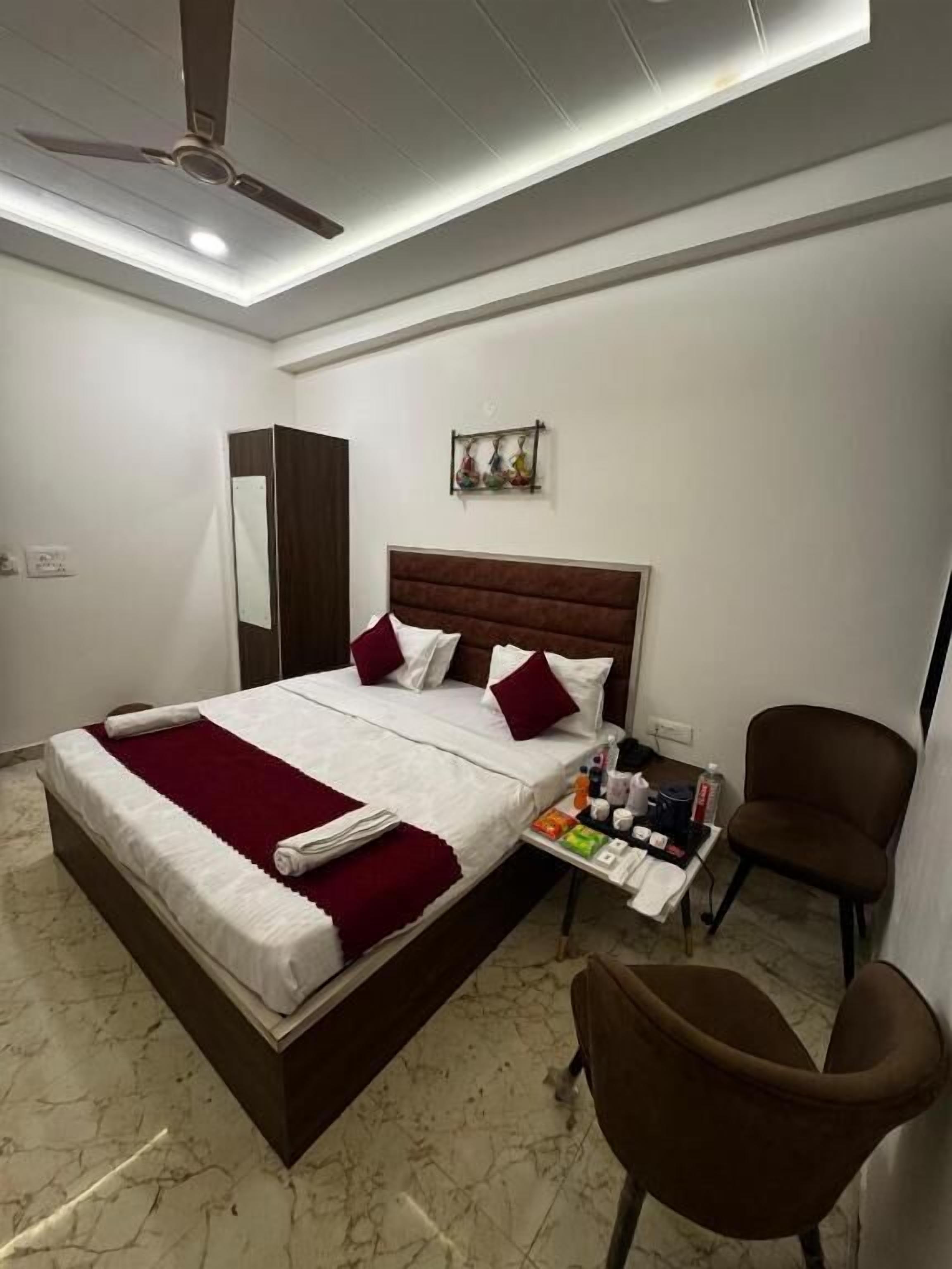 A hotel room with a bed, a ceiling fan, a small table with toiletries, and a brown chair.