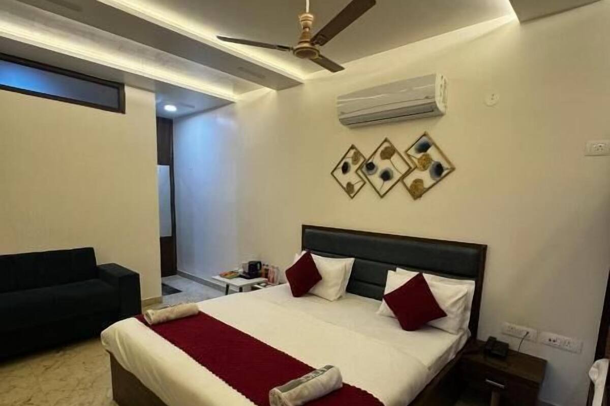 A modern hotel room with a large bed, a ceiling fan, an air conditioning unit, and a small bedside table.