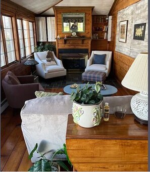 Ein gemütlicher Raum mit Kamin, zwei Sesseln, einem Sofa, einem Couchtisch und einem Beistelltisch mit Lampe und einer Flasche.
