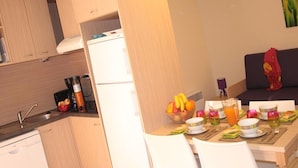 A compact kitchen with a refrigerator, a dining table set with plates, glasses, and a fruit bowl. - Spacious Beachside Apartment for 6 (Saint-Cyprien)