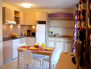 A compact kitchen with modern appliances, a dining table set for two, and a small refrigerator. - Spacious Beachside Comfort for 6 (Saint-Cyprien)