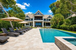Ein zweistöckiges Haus mit Swimmingpool, Sitzgelegenheiten im Freien und üppiger Bepflanzung.