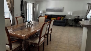 Zona pranzo con tavolo e sedie in legno, un divano con cuscini, una lampada e una luce a soffitto.