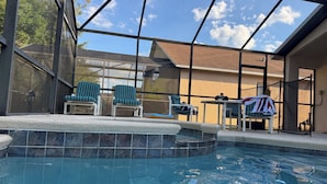 Una piscina con recinto in vetro, due sedie, un tavolo e una sedia con copertura.