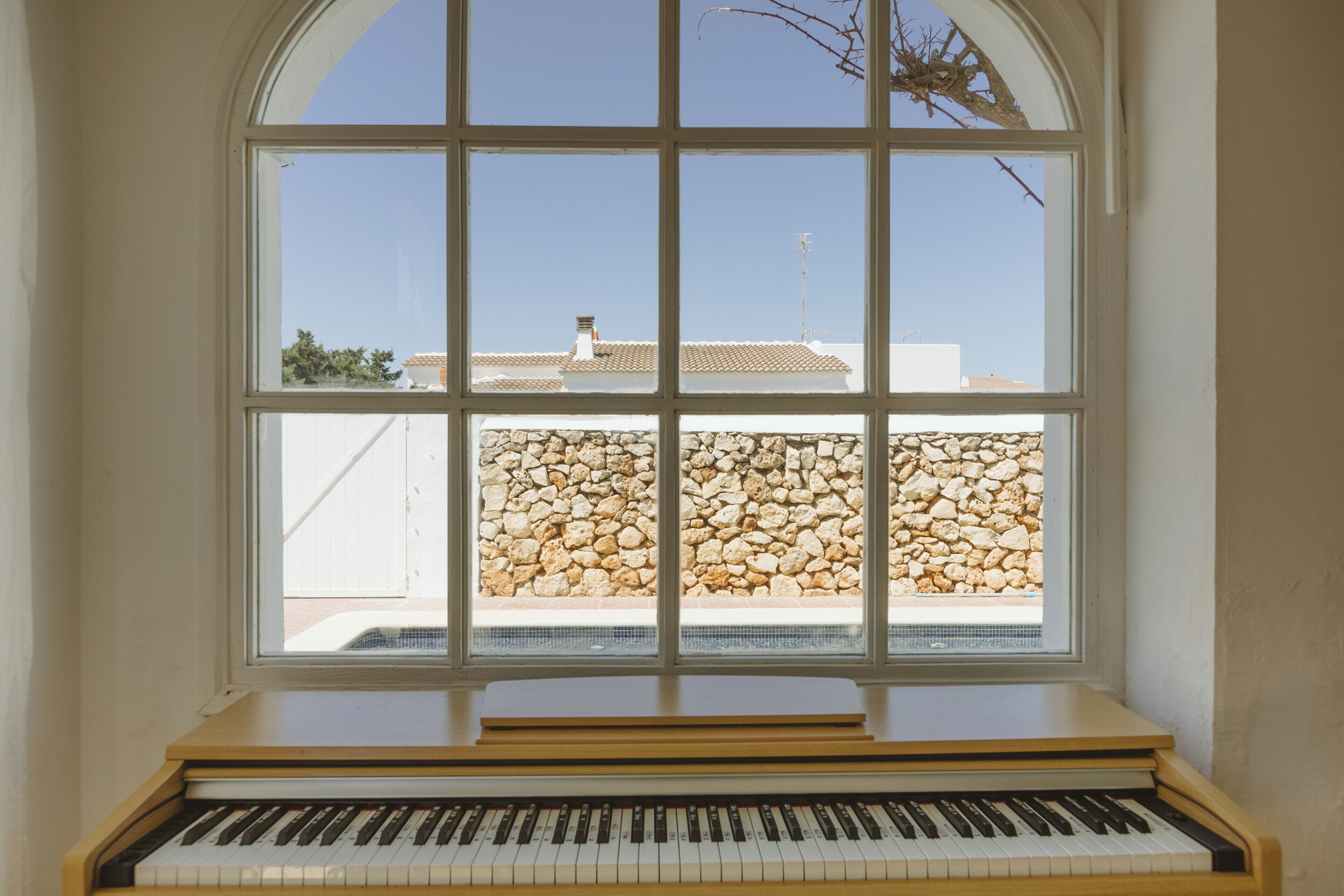 Ein Klavier in einem Raum mit einem großen Bogenfenster mit Blick auf eine Steinmauer und Gebäude.