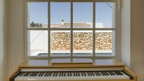 Un piano en una habitación con un amplio ventanal que da a un muro de piedra y edificios.