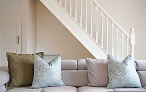 A living room with a sofa, two pillows, a staircase, and a white door. - The Green - Stylish Home Sleeps 6 With Parking (York)