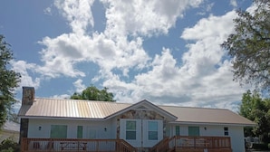 A two-story building with a stone facade, a metal roof, and a wooden deck with a staircase. - Reel Em' Inn -3bdr 2.5ba Waterfront Home Located at Pier98 Marina -Pets Welcome (Panama City)