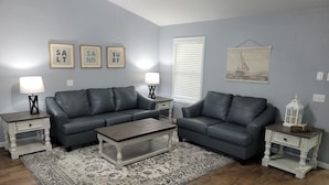 A living room with two sofas, a coffee table, and a patterned rug. There are framed words on the wall and a sailboat painting. - Reel Em' Inn -3bdr 2.5ba Waterfront Home Located at Pier98 Marina -Pets Welcome (Panama City)