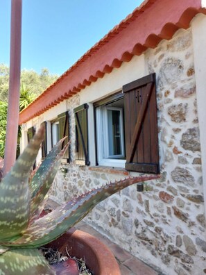 A stone building with a red-tiled roof and windows with dark shutters. - Small house with swimming pool and parking, in a quiet location close to the beach. (Antibes)