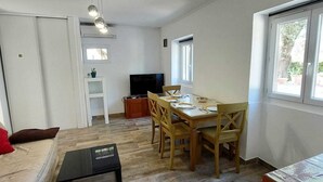Ein Wohnzimmer mit einer Couch, einem Couchtisch, einem Esstisch mit Stühlen, einem Fernseher und einem Fenster.