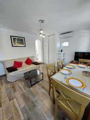 Un salon avec un canapé, une table à manger dressée pour quatre personnes et un téléviseur.