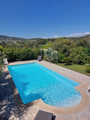 Une piscine rectangulaire à bords incurvés, entourée de carreaux de pierre et de verdure.