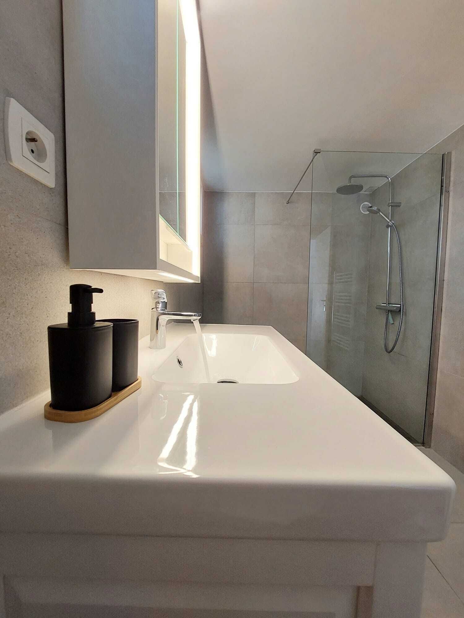 Ein modernes Badezimmer mit Waschbecken, Spiegel, Dusche und einer Leuchte.