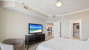 Un dormitorio con una cama grande, televisión, una silla y un baño visible a través de una puerta abierta.