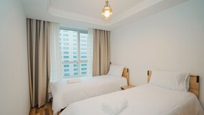 Ein Hotelzimmer mit zwei Betten, einem Holzkopfteil, einem großen Fenster mit Vorhängen und einer Deckenleuchte.