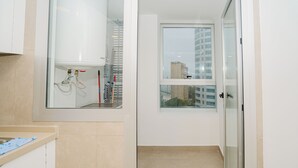 Ein helles, modernes Badezimmer mit Glasdusche, einem Fenster mit Blick auf die Stadt und einem sichtbaren Warmwasserbereiter.