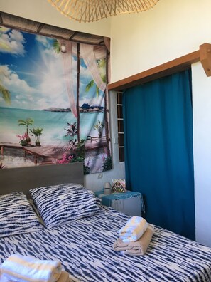 A bedroom with a bed, pillows, a blue curtain, and a tropical mural on the wall. - Accommodations in a farmhouse with a private entrance (no common areas) (Pertuis)