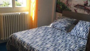 A bed with a patterned bedspread, a window with curtains, a radiator, and a beach mural on the wall. - Dwelling in farmhouse with independent entrance (no shared rooms) (Pertuis)