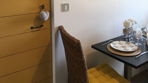 A room with a wooden door, a wicker chair, a small table with a plate and glasses, and a framed painting on the wall. - Dwelling in farmhouse with independent entrance (no shared rooms) (Pertuis)