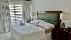 Ein ordentlich bezogenes Bett mit weißen Leinen, einem mit Grün bezogenen Kopfteil und zwei Nachttischlampen.