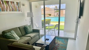 Ein Wohnzimmer mit einer Couch, einem Couchtisch, einem Fernseher und Blick auf einen Pool.