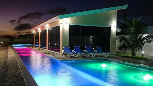 Ein Schwimmbecken im modernen Design, umgeben von Liegestühlen und einem überdachten Bereich mit Glaswänden.
