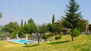 Ein Pool mit Liegestühlen, ein Steinhaus und ein Hügel mit Bäumen.