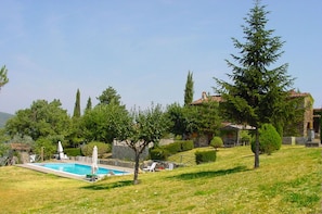 Ein Pool mit Liegestühlen, ein Steinhaus und ein Hügel mit Bäumen.