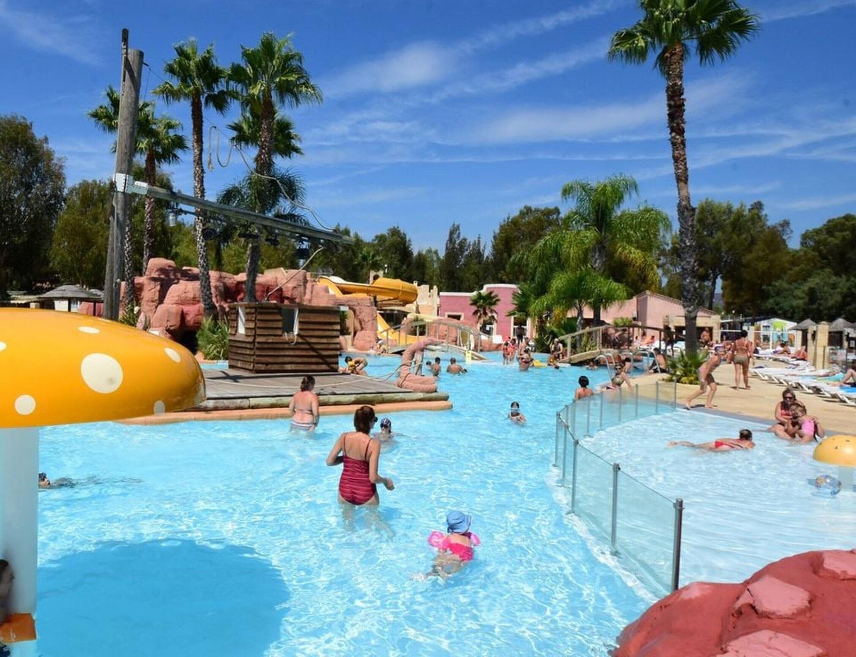 A swimming pool area with multiple water slides, palm trees, and a rock formation.