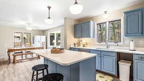 A kitchen with a central island, bar stools, and blue cabinets. - Leonards Cabin on Round Lake | Private Dock, 140ft Shoreline, Close to Town - New Rental (Hayward)